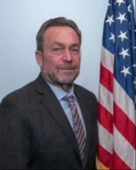 Richard Brewer, Jr., Town Councillor At-Large standing by an American Flag